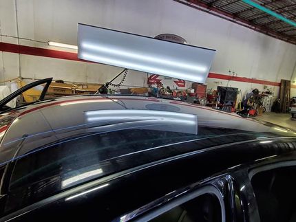 Black car roof with a dent repair light, inside a garage.