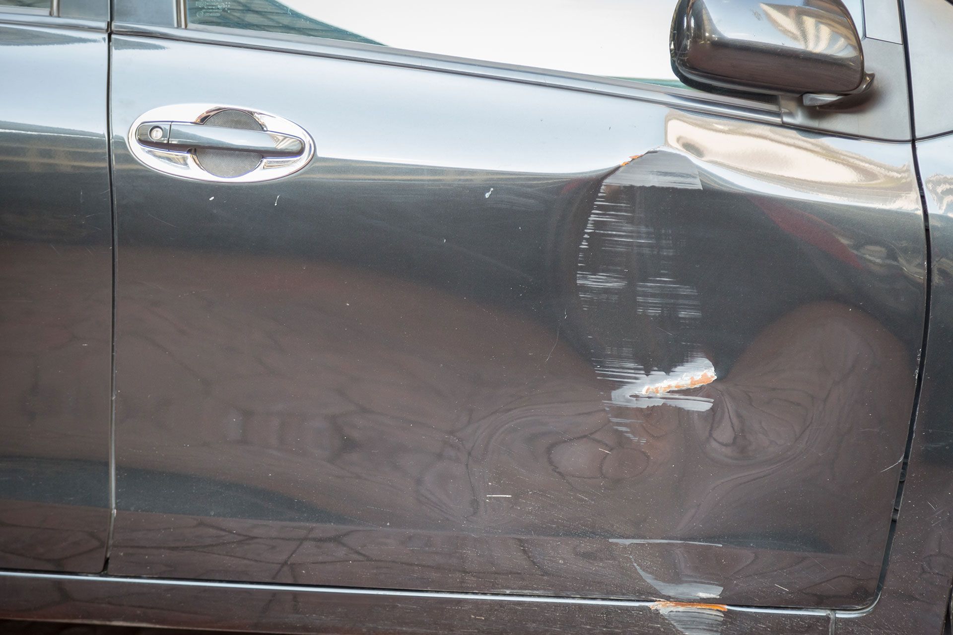 Damaged black car door with scratches and a dent, likely from a collision.