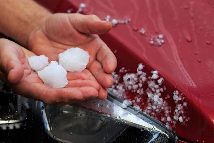 Hands holding hailstones on a red car hood, after a hailstorm.