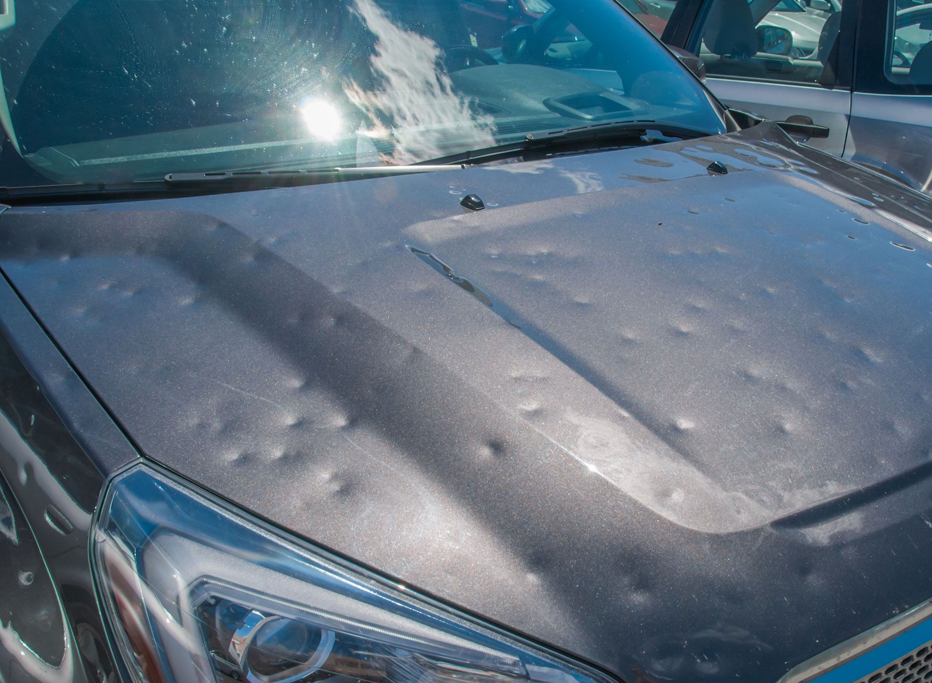 Gray car hood damaged by hail with multiple dents.