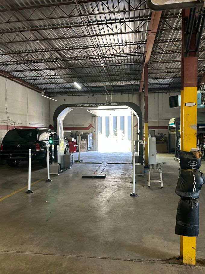 Interior of a car wash bay. Black SUV waits near a white archway leading to the outside.