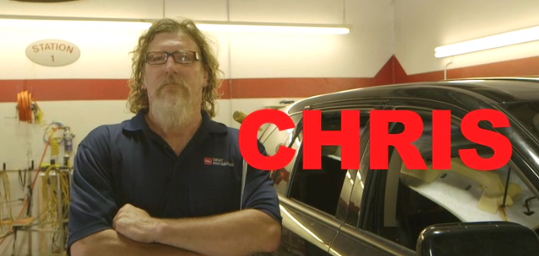 Chris in a garage with a black vehicle, arms crossed. Red text 