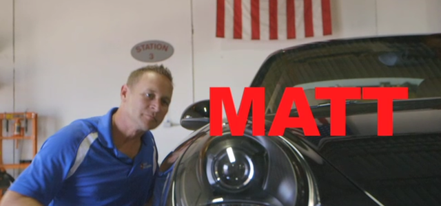 Man in blue shirt stands next to black car; red letters spell 