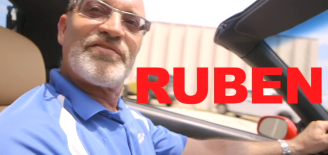 Man named Ruben in a car, wearing glasses and a blue shirt, with 