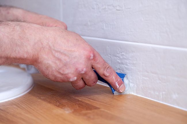 someone sealing the gap between the flooring and the wall