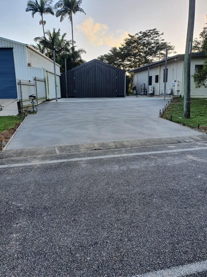 A Concrete Driveway Leading to a Building With a Shed in the Background — Bark Concreting In Ryan, QLD