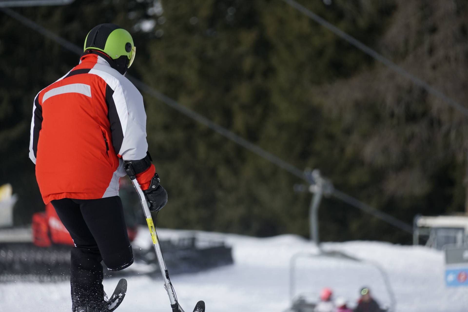 A lower limb amputee in a red ski coat skiing in a snowy landscape.