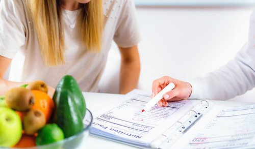 A woman is sitting at a table with a bowl of fruit and vegetables.