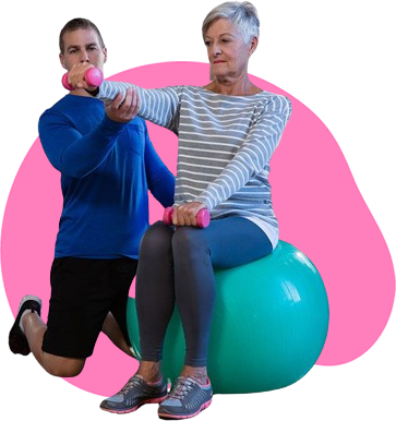 A man is helping an older woman lift dumbbells while sitting on an exercise ball.