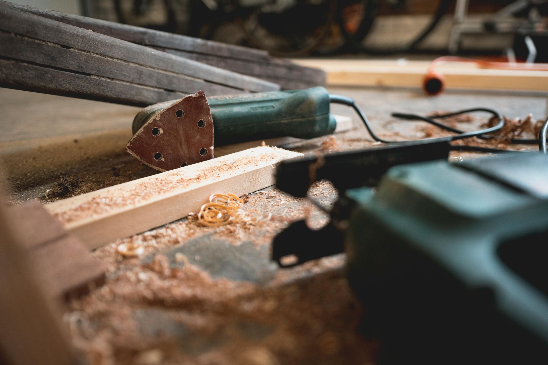 Green power tools, including a sander and jigsaw, amidst wood shavings and lumber.