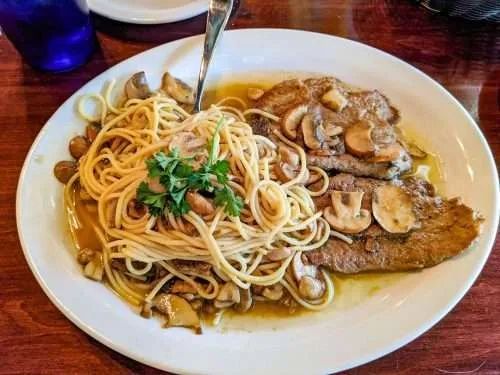 Plate of spaghetti with mushrooms, breaded cutlets, and sauce.