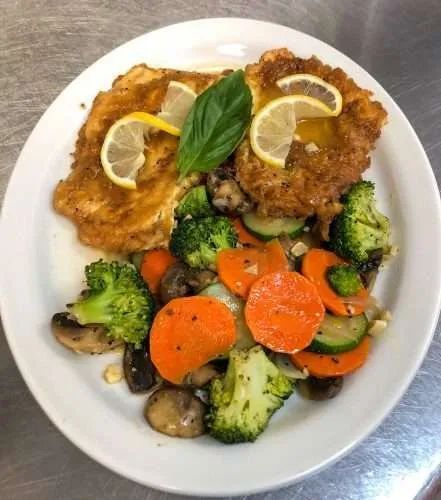 Chicken cutlets with lemon and vegetables on a white plate.