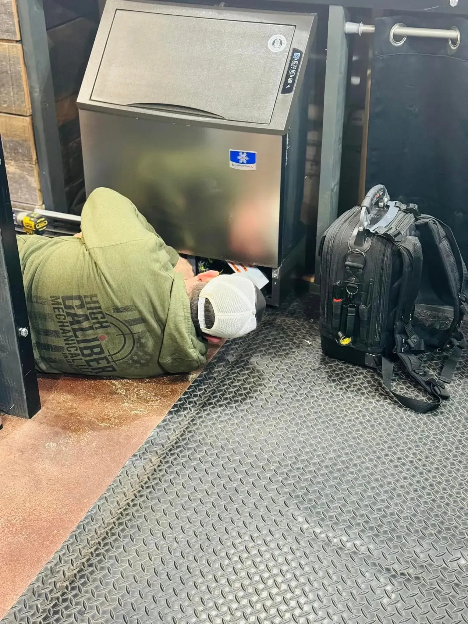 A man is laying on the floor next to a refrigerator.