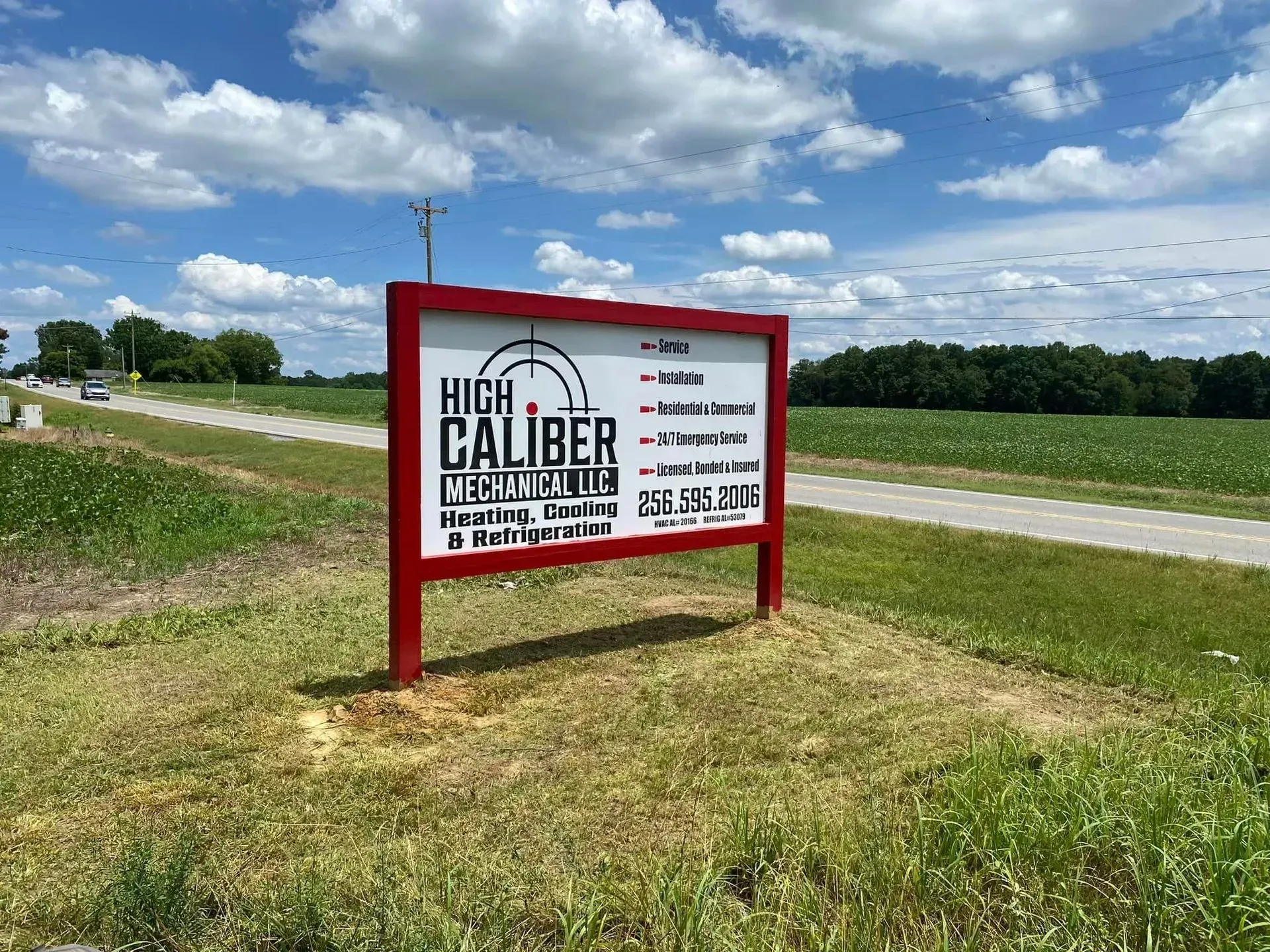 A red and white sign is sitting in the middle of a grassy field next to a road.