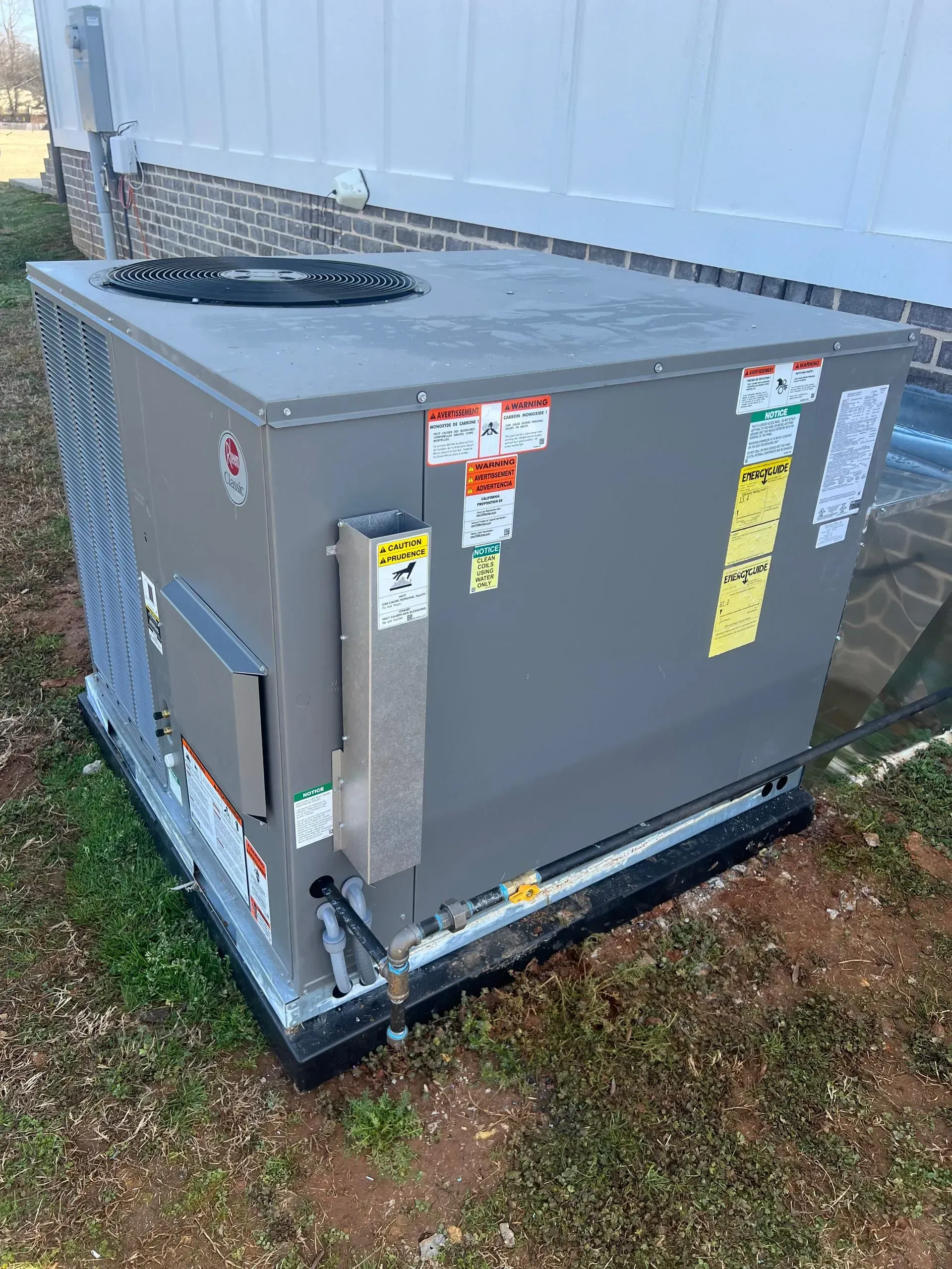A large air conditioner is sitting in the grass in front of a house.
