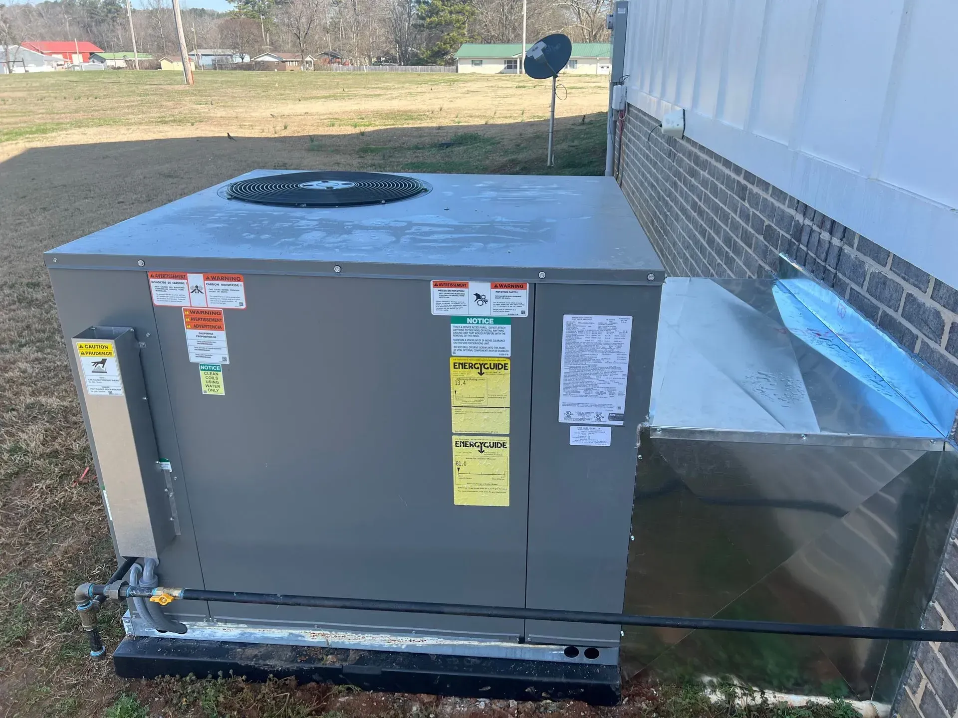 A large air conditioner is sitting outside of a brick building.