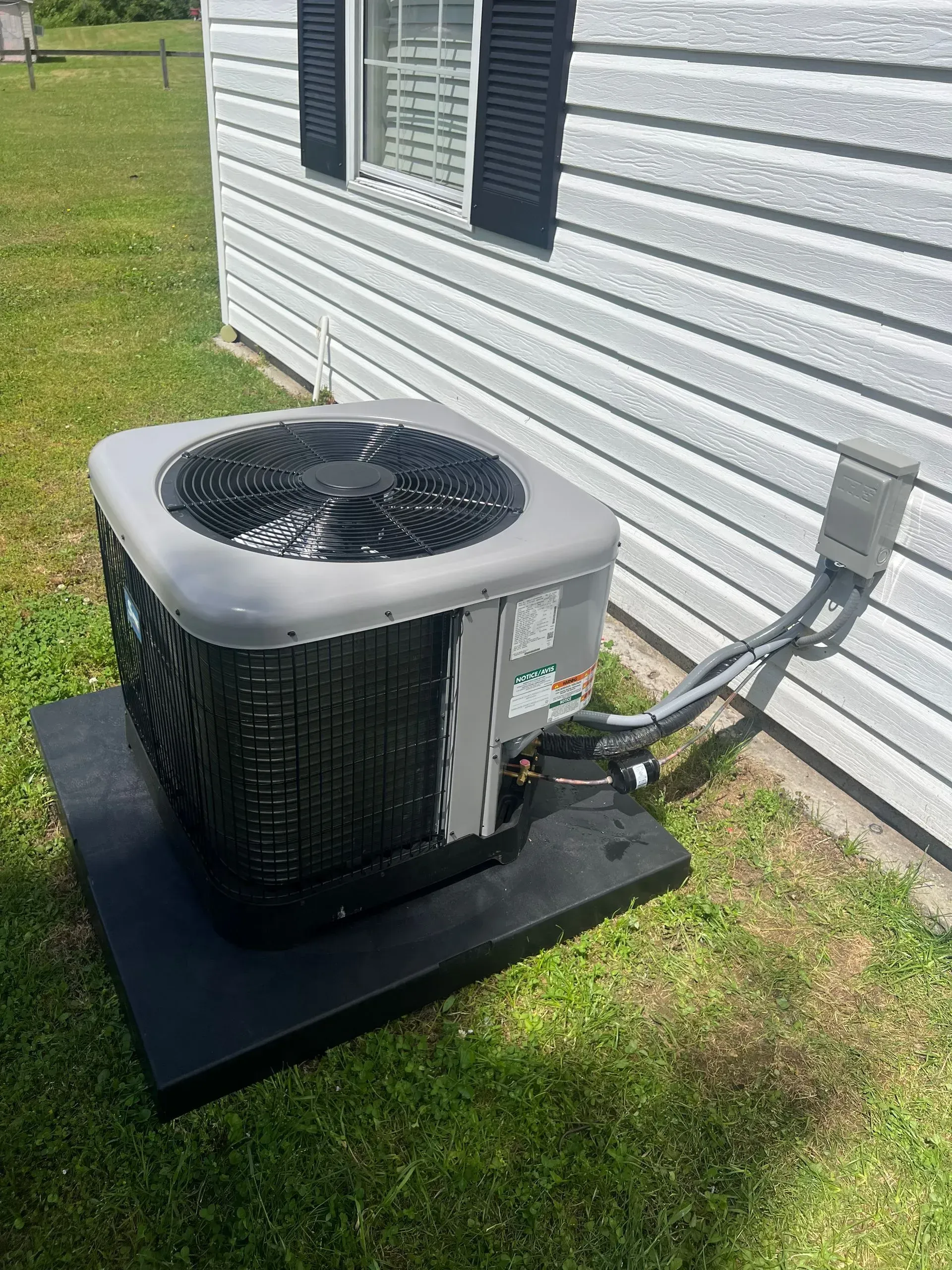 An air conditioner is sitting on top of a black platform in front of a house.