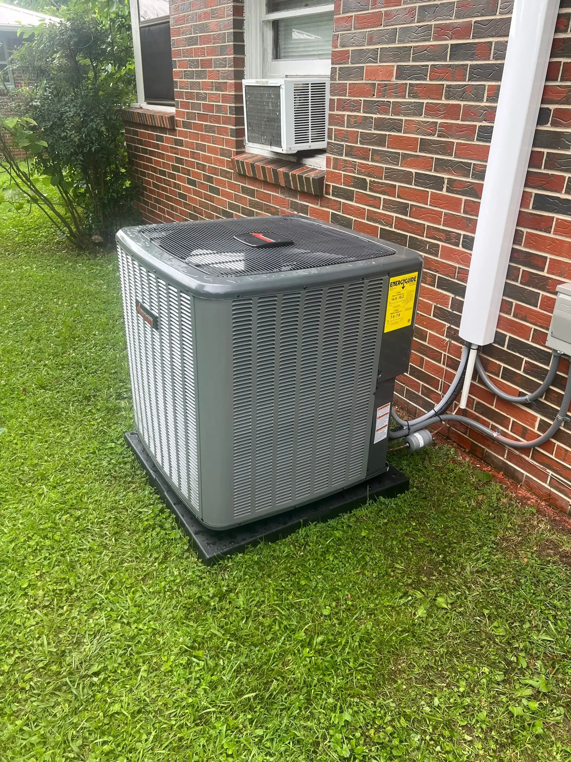 A large air conditioner is sitting on top of a lush green lawn in front of a brick building.