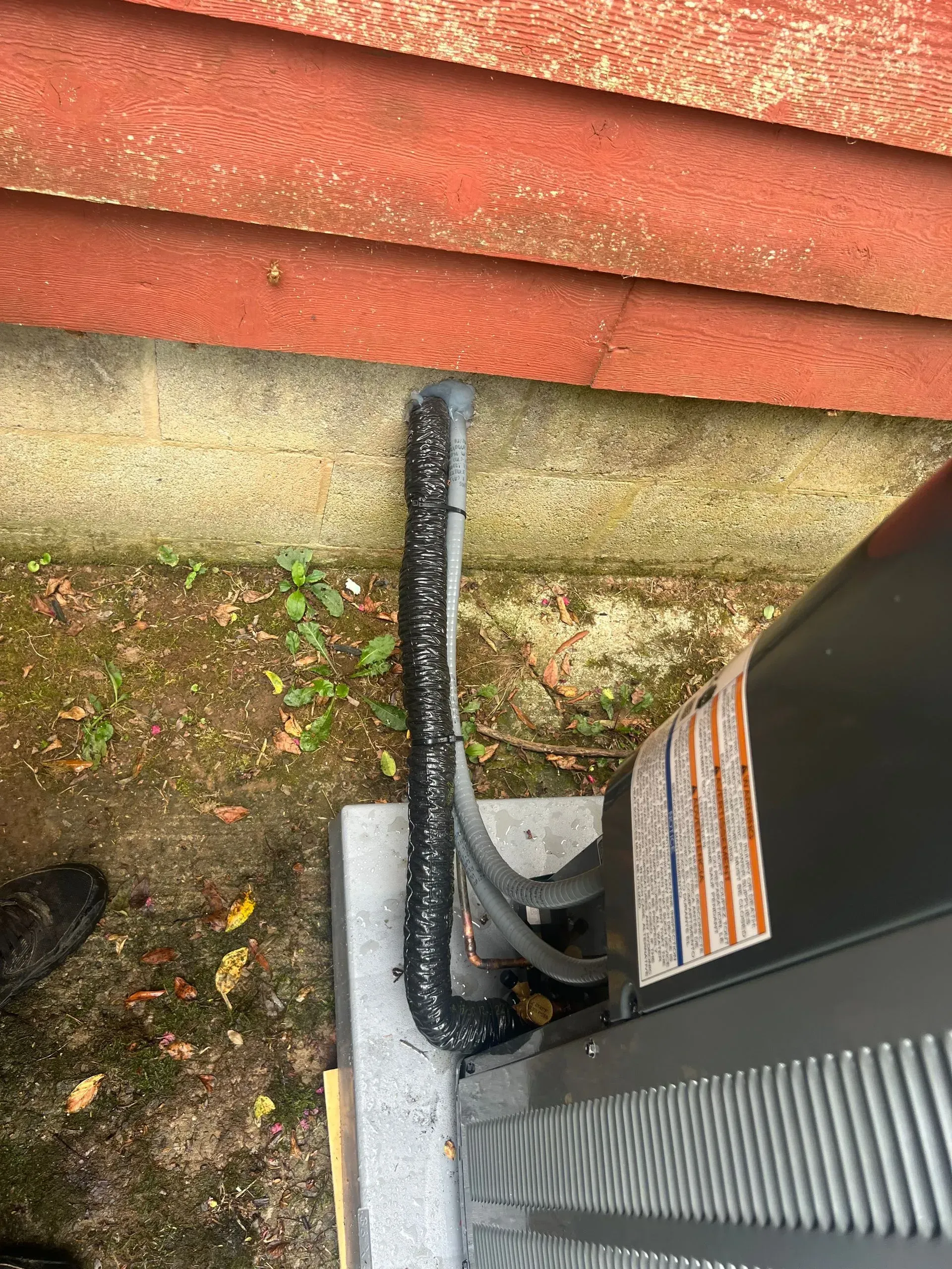 A black air conditioner is sitting on the ground next to a red wall.