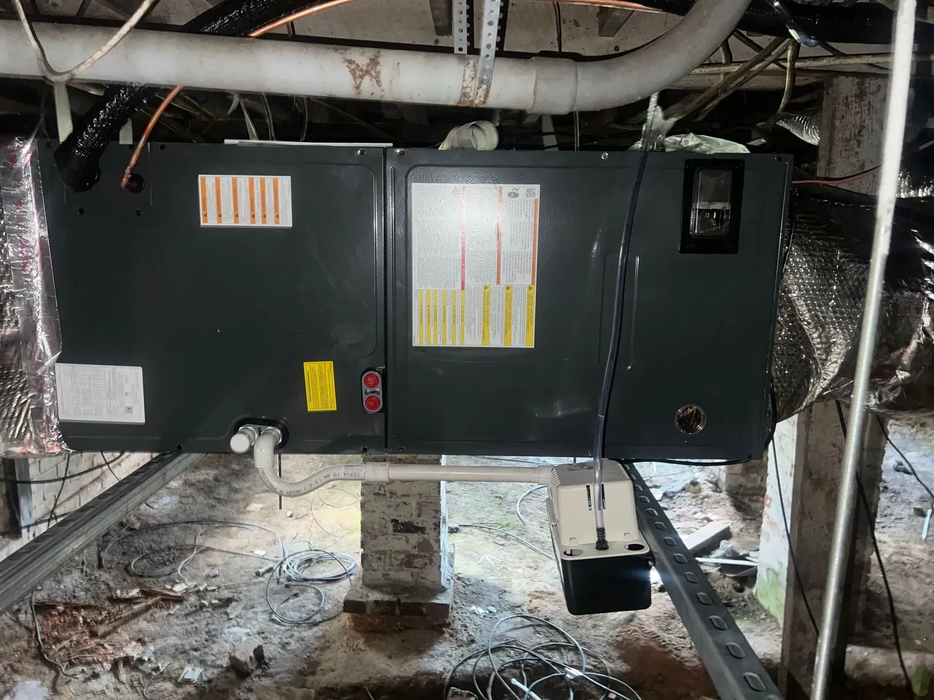 An air conditioner is sitting under a ceiling in a basement.