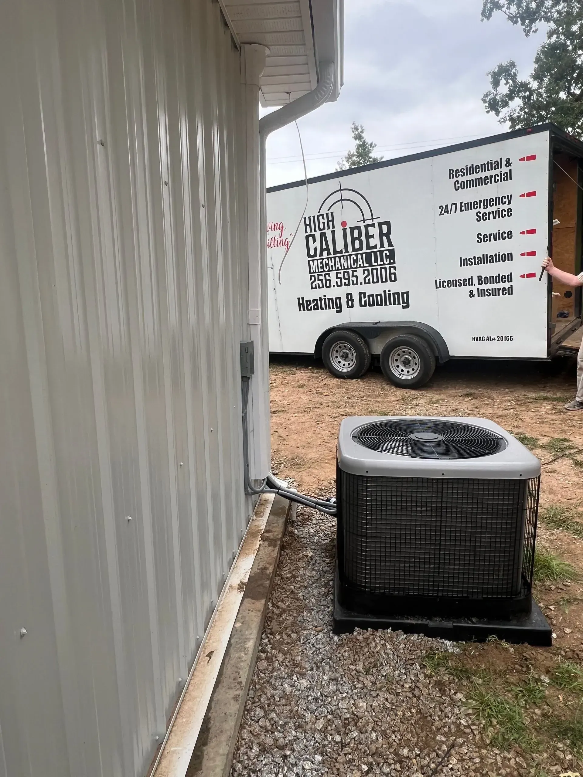 A white trailer is parked next to a house with an air conditioner.