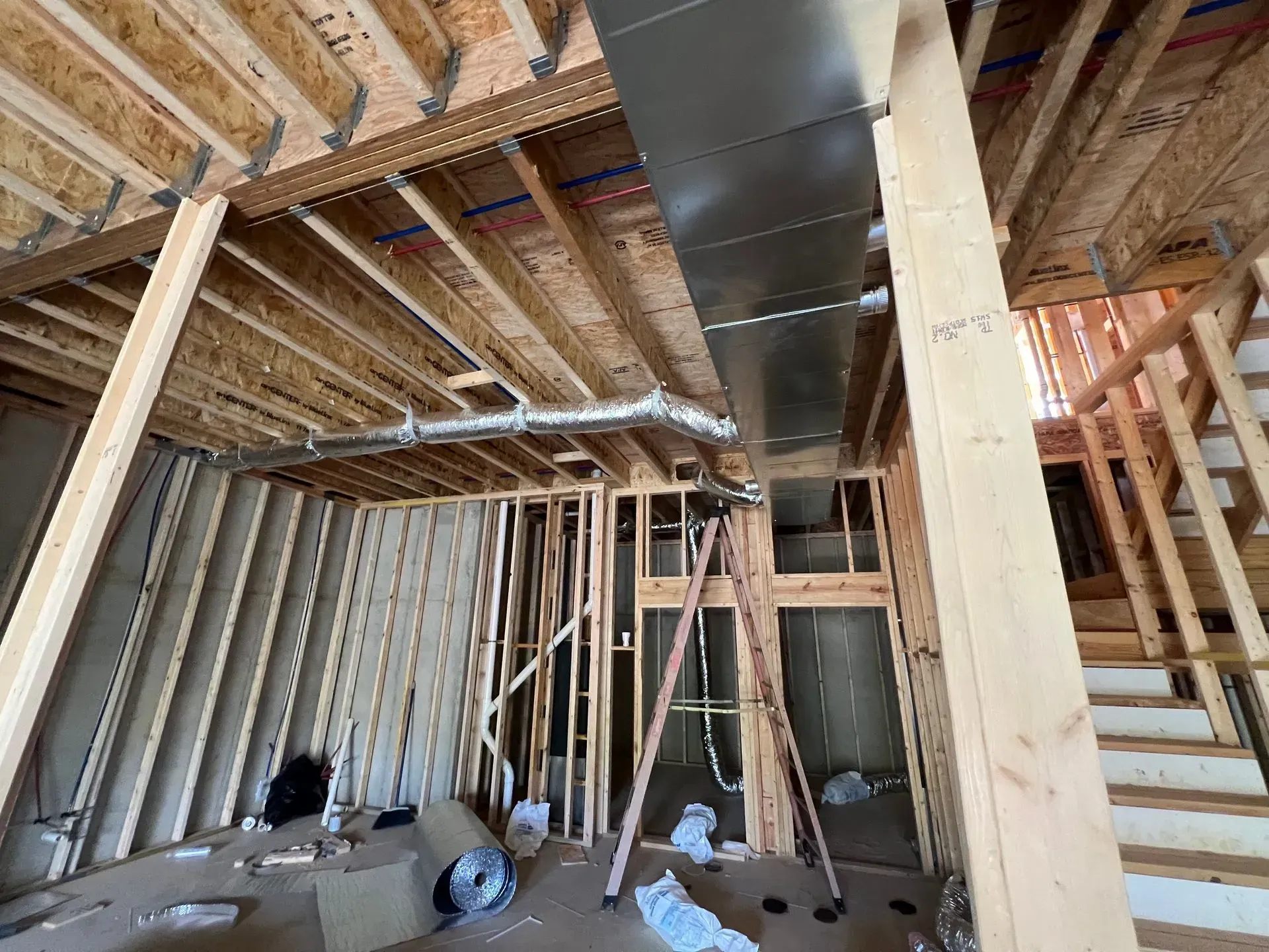 A room in a house under construction with a metal duct hanging from the ceiling.