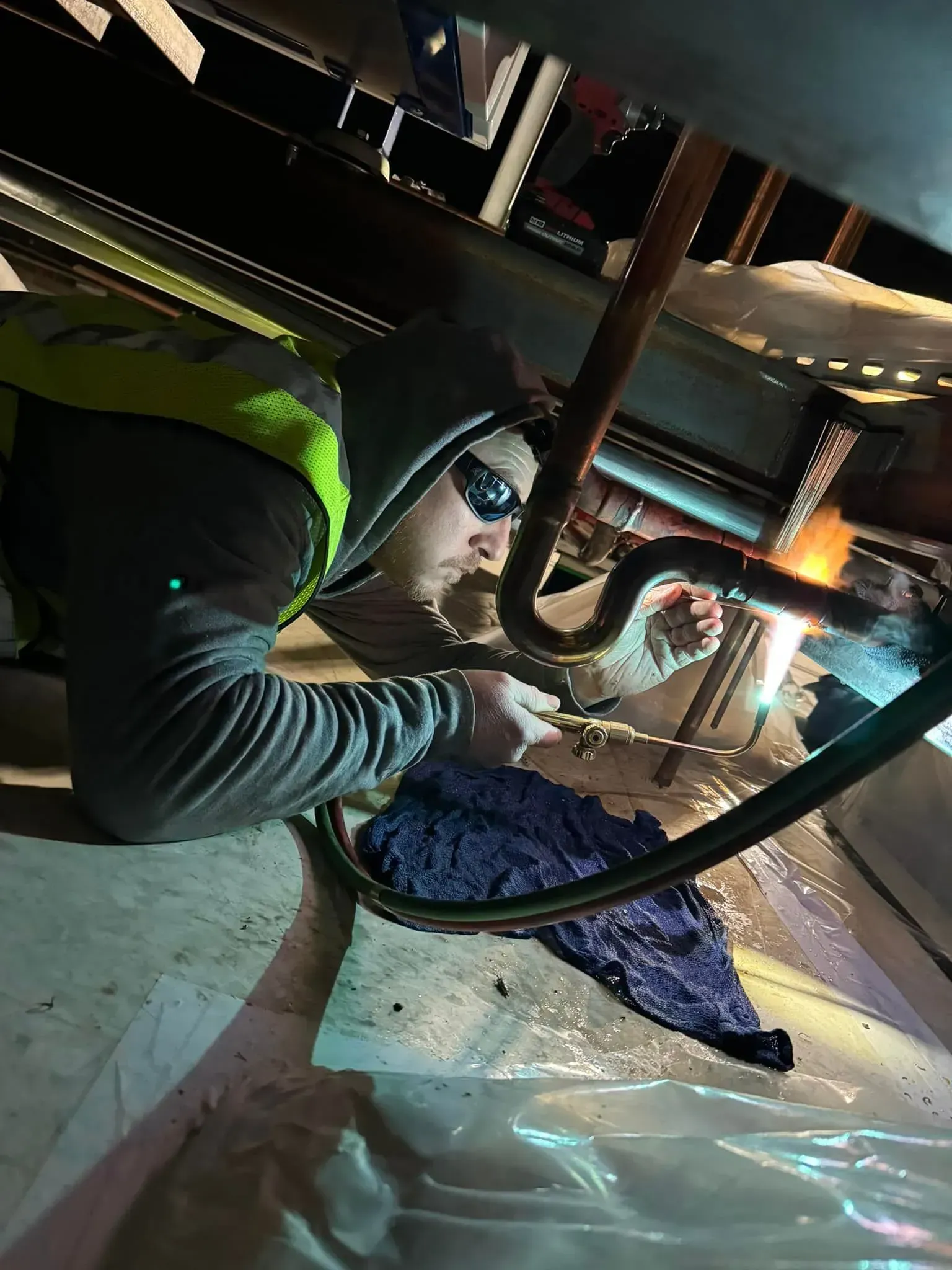 A man is working under a pipe with a flashlight.