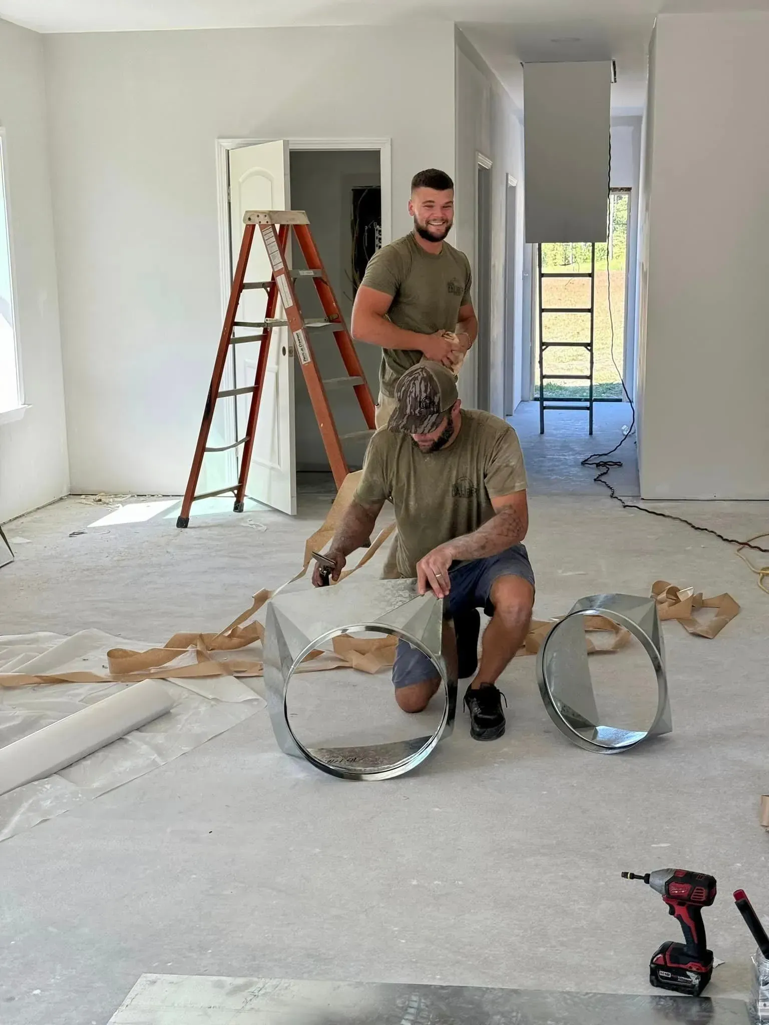 Two men are working on a metal ring in a room.