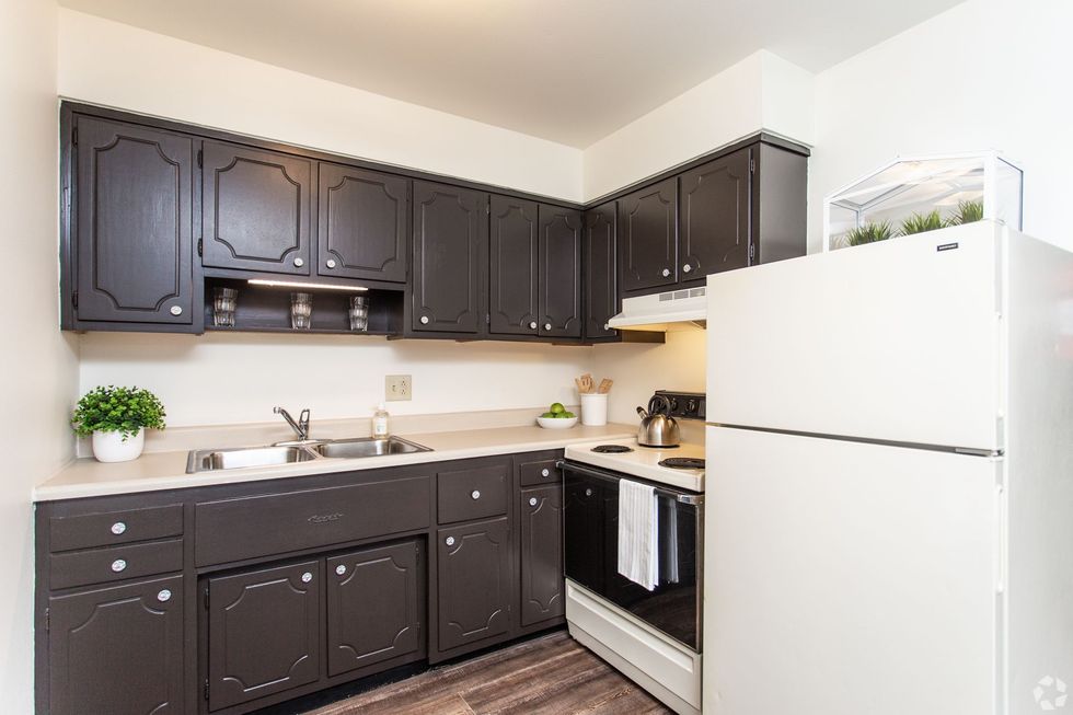 A kitchen with black cabinets , a white refrigerator , a stove , and a sink.
