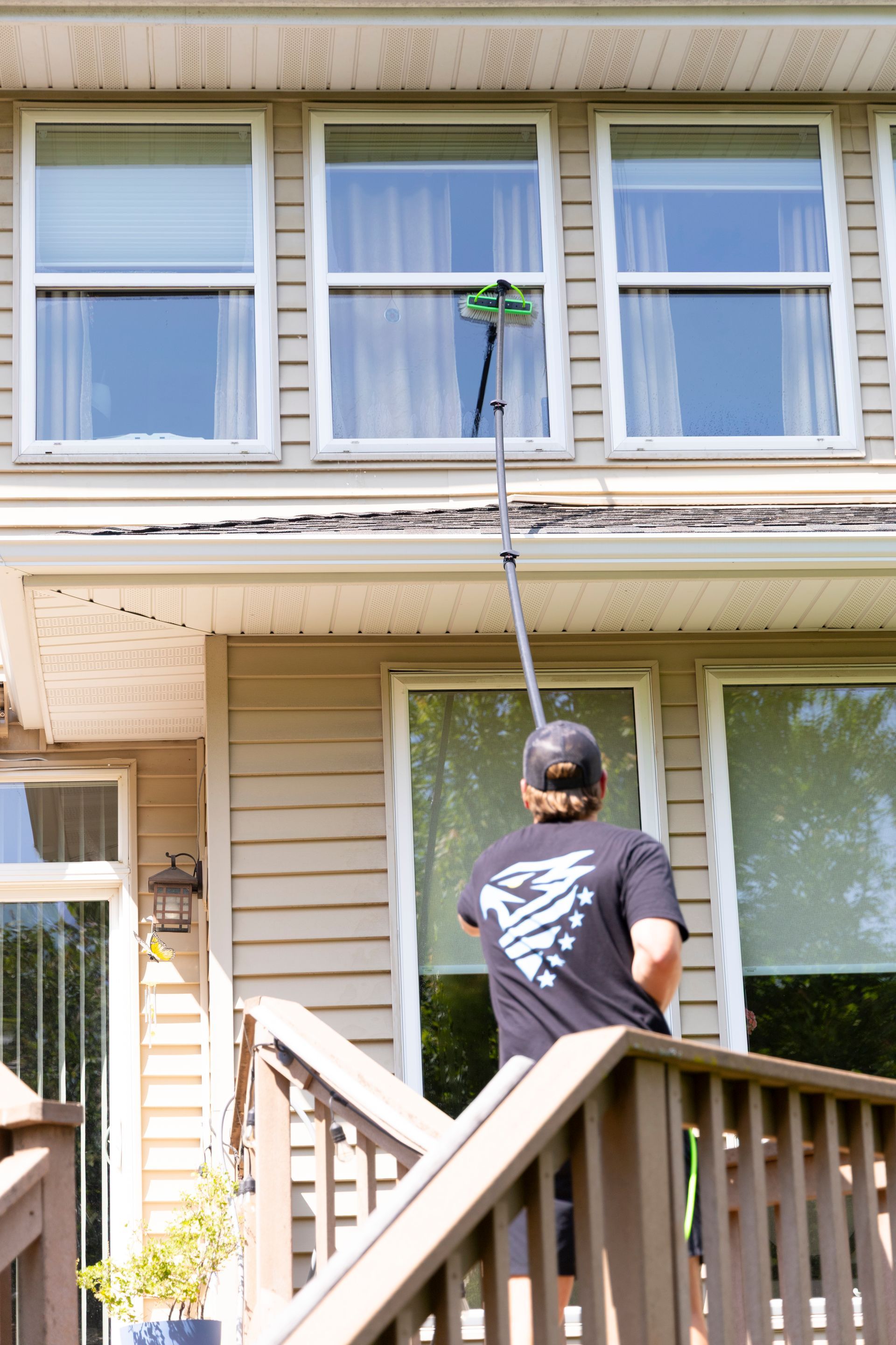 A man is cleaning the windows of a house with a pole.