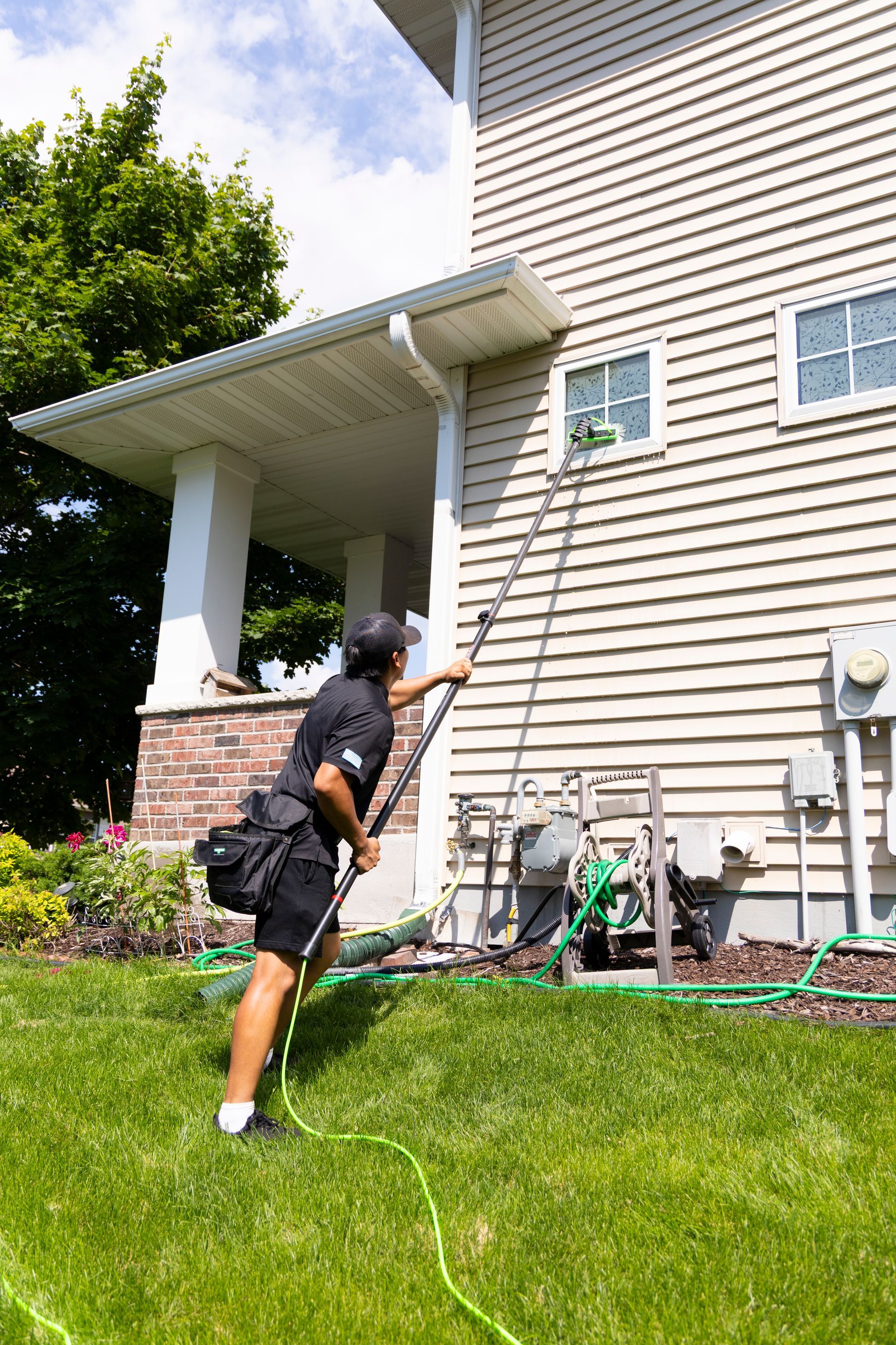 A man is cleaning the windows of a house with a pole.