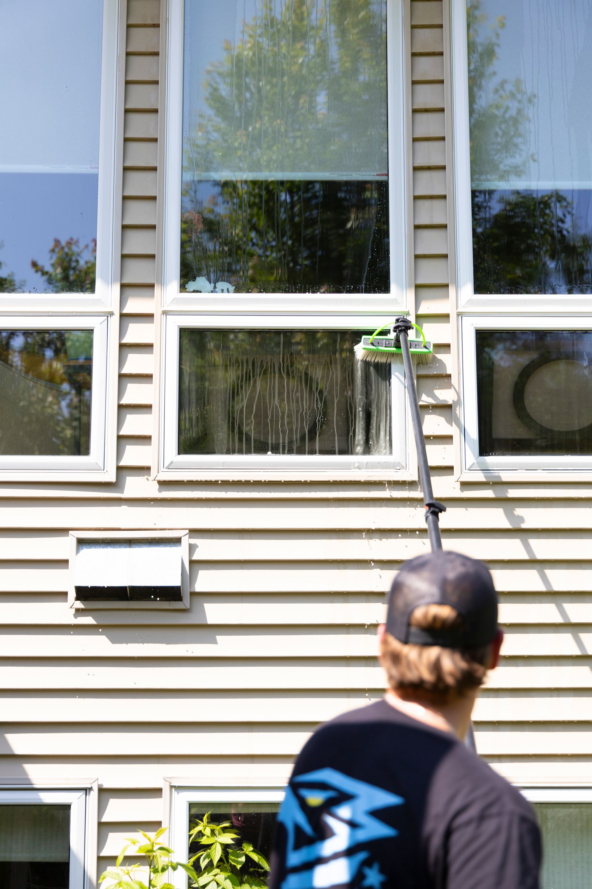 A man is cleaning the windows of a house with a pole.