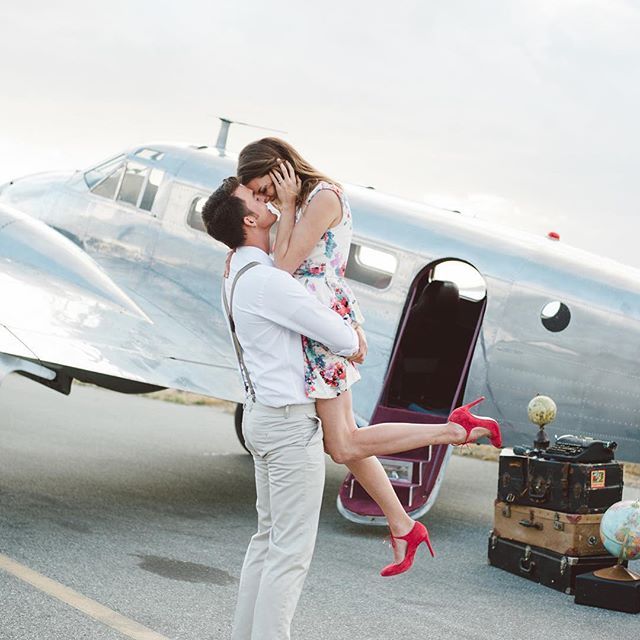 A man and woman kissing in front of an airplane