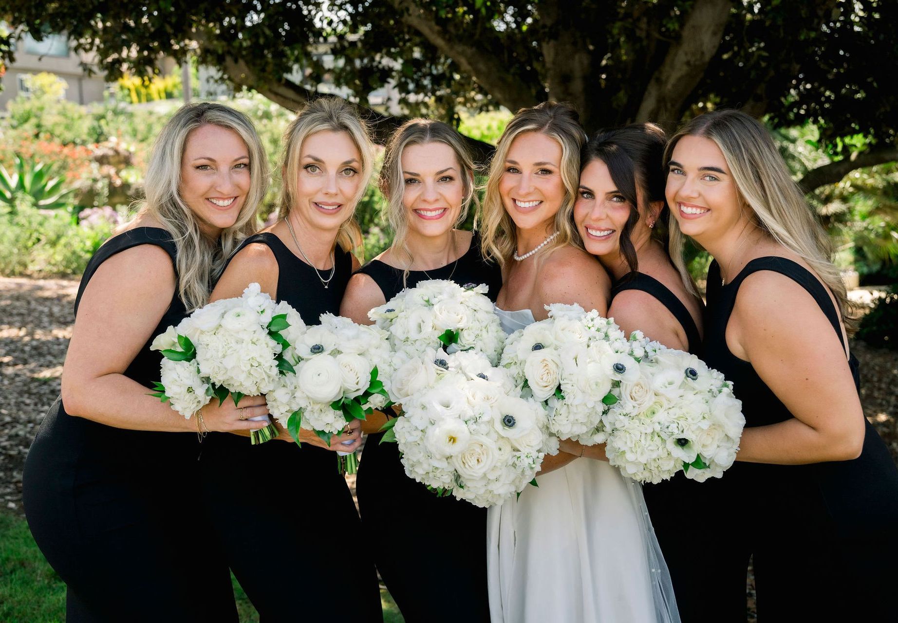 A bride and her bridesmaids are sitting on a bed drinking champagne.