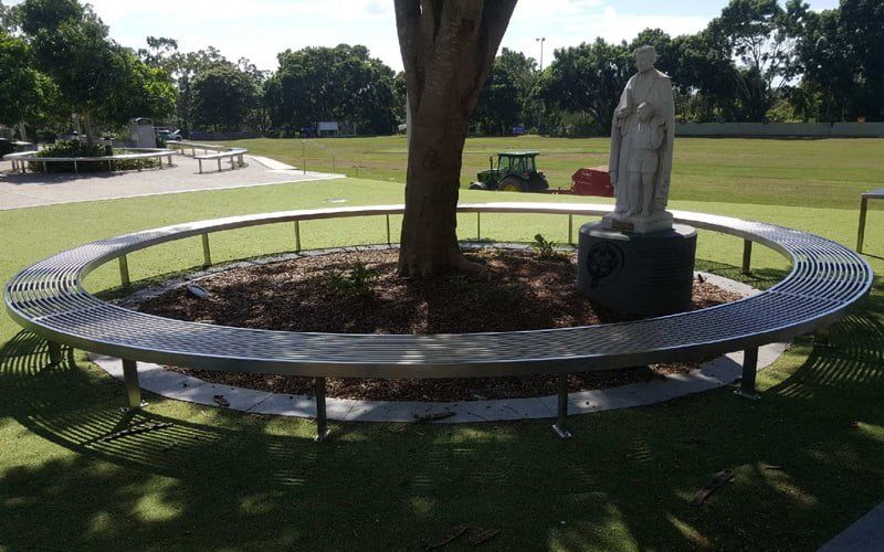 Circular stainless steel bench around a tree and a statue