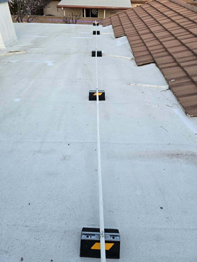 A long, white pipe mounted on black, rectangular bases stretches across a flat, gray roof next to a sloped tiled roof.