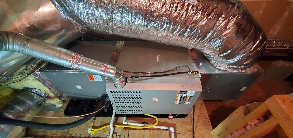 An HVAC air handler unit installed in an attic, connected to insulated silver flexible air ducts and PVC drain piping.