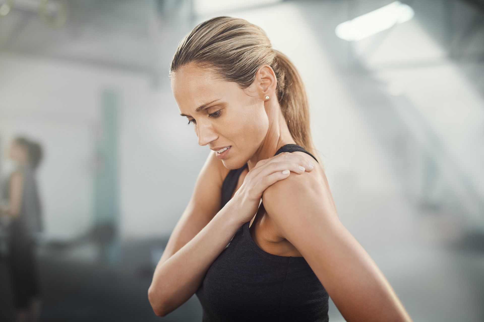 Woman in a gym clutches her shoulder, exhibiting a pained expression; likely injured.