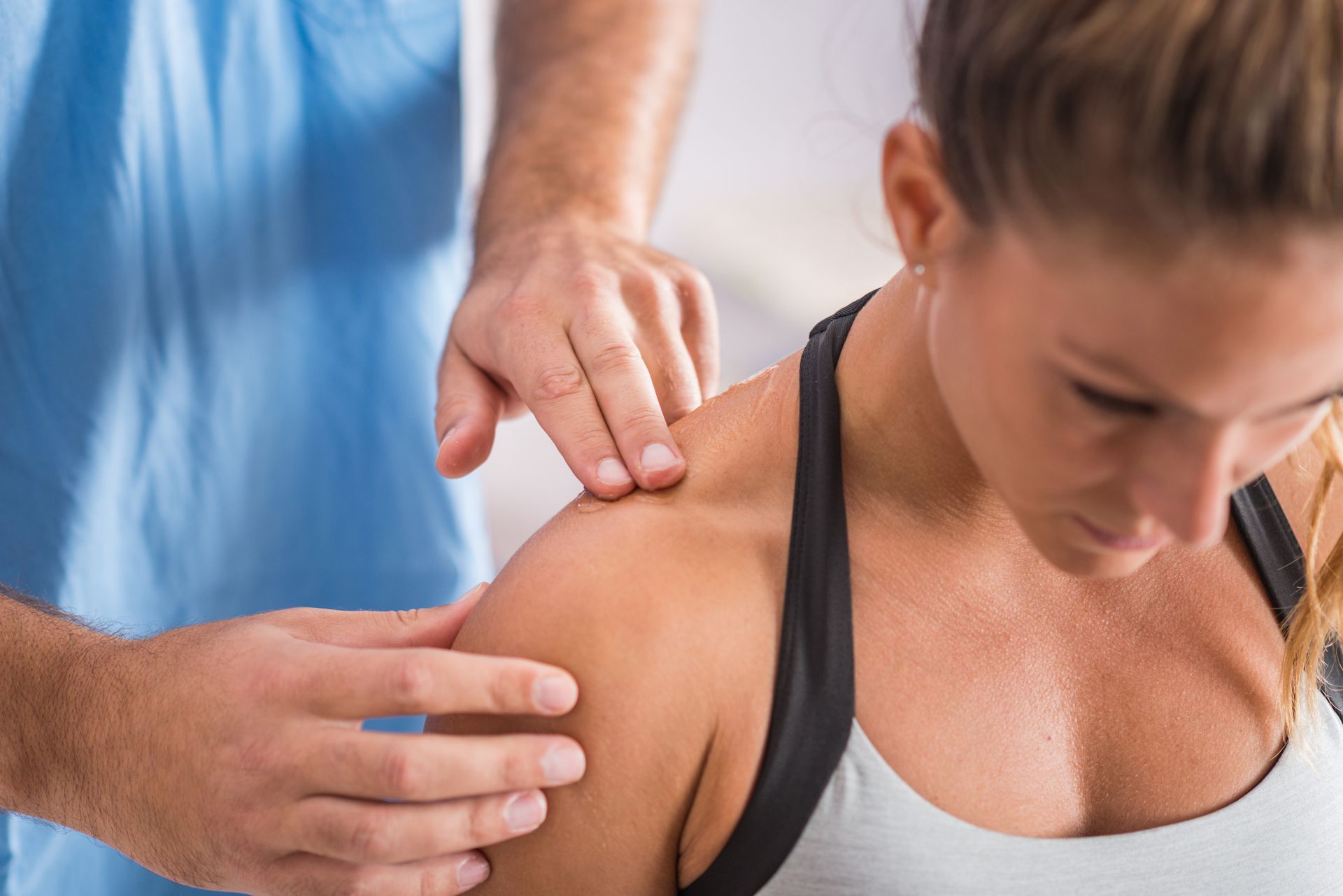 A healthcare professional examines a woman's shoulder. The woman is looking down, possibly experiencing pain.