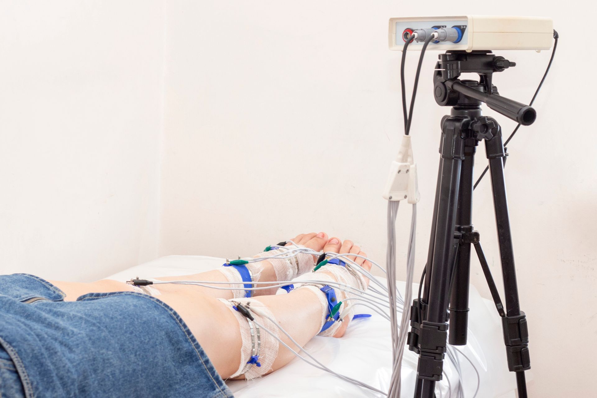 Person undergoing a medical test with electrodes attached to their legs, equipment nearby, and a tripod.