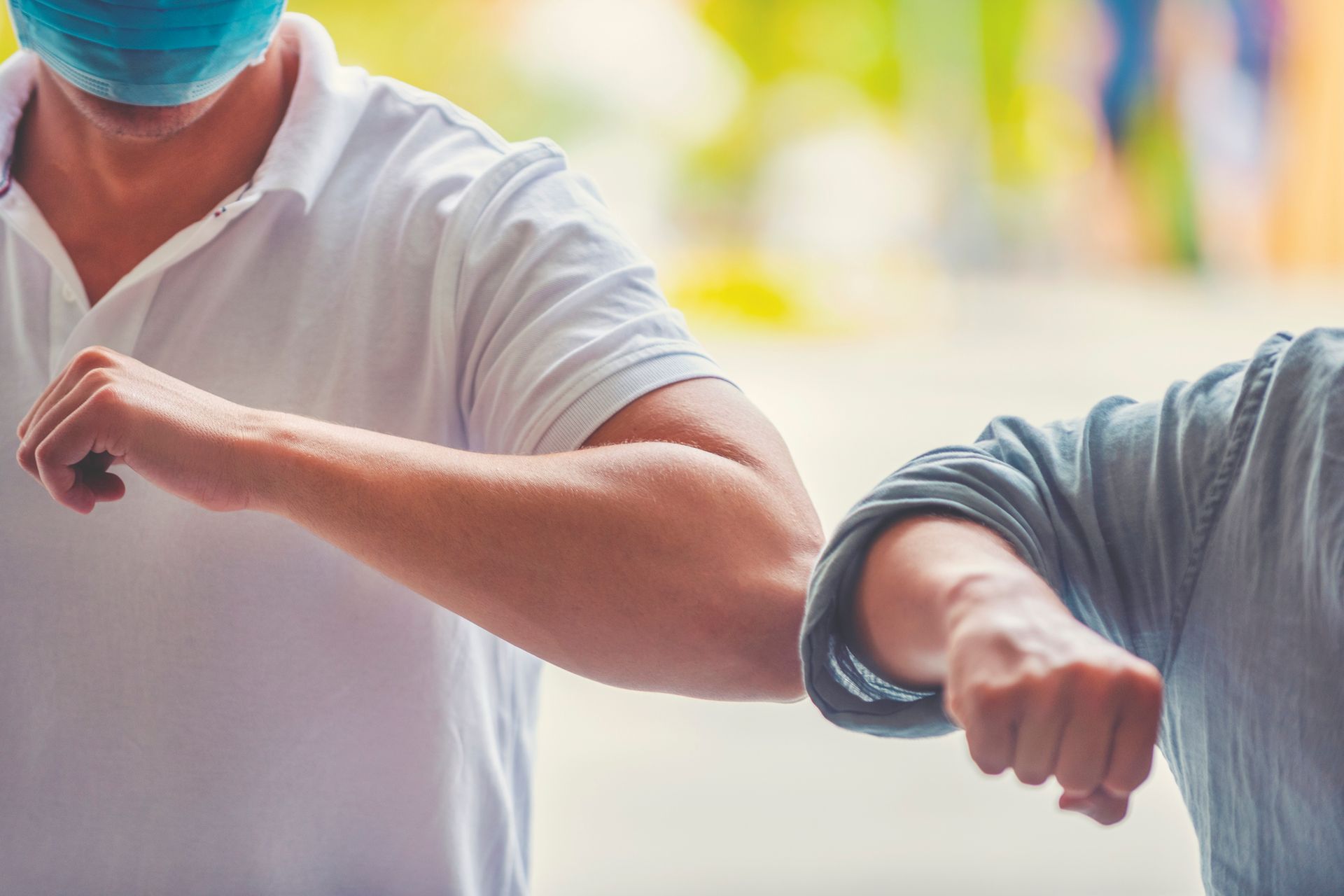Two people, one wearing a face mask, touch elbows as a greeting, possibly to prevent the spread of germs.