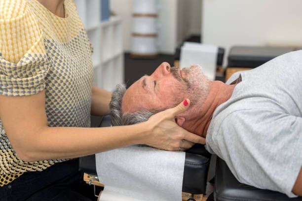 A chiropractor adjusting a man's neck. The man lies face-up on a chiropractic table, the doctor's hands on his head.