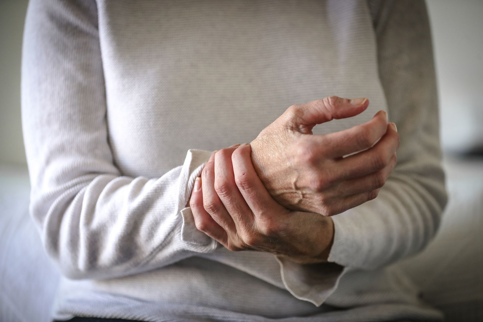 Woman holding wrist, indicating pain; wearing white long-sleeved shirt.