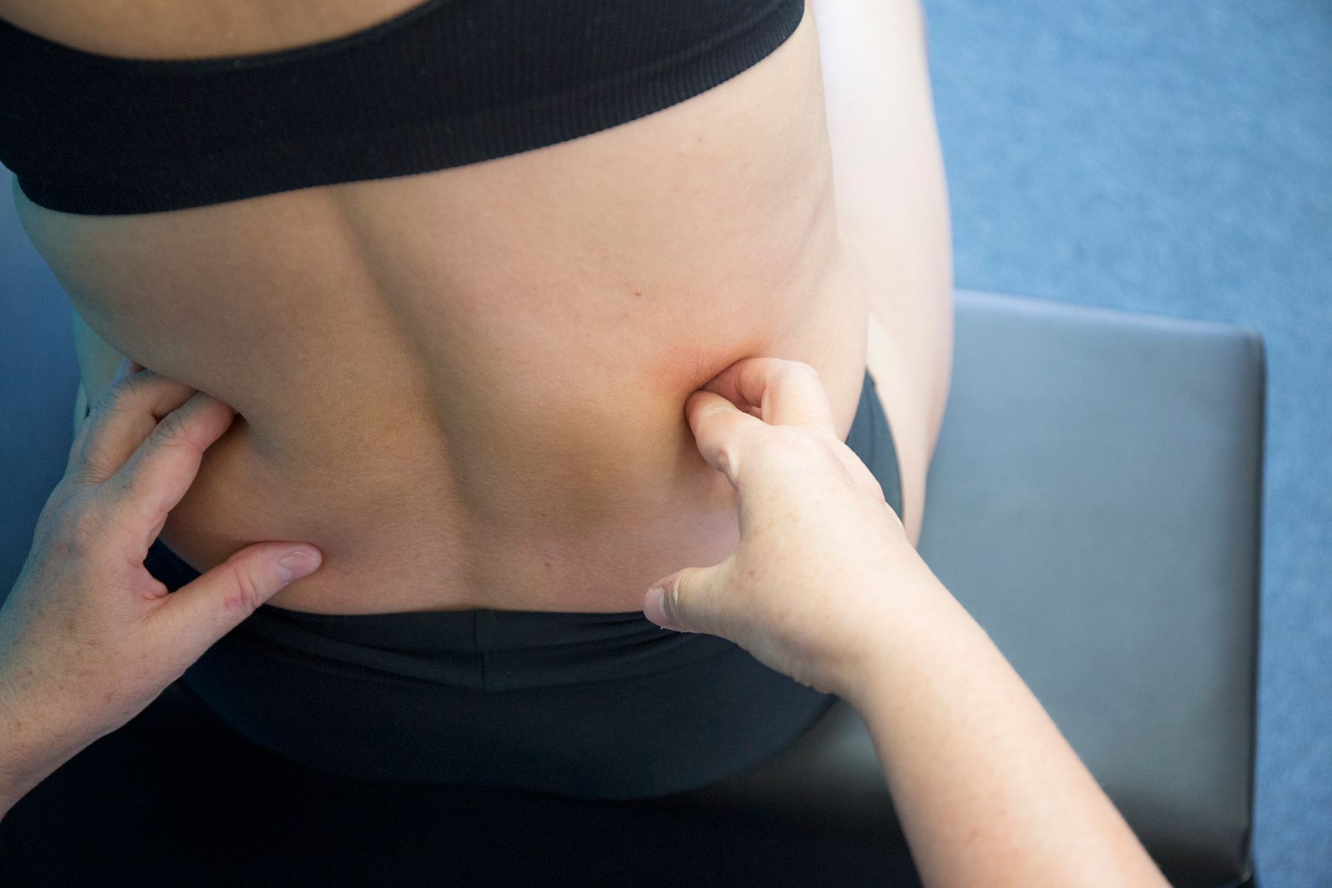 Hands palpating the lower back of a person wearing black athletic clothing.