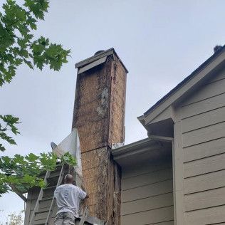 A man is standing on a ladder next to a chimney on the side of a house 