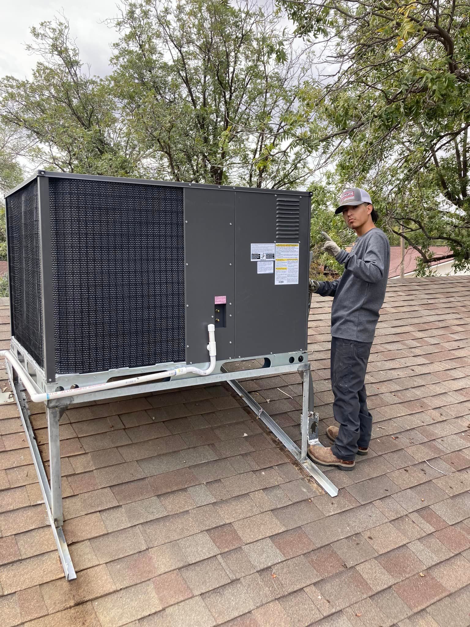 A man is standing on top of a roof working on an air conditioner.