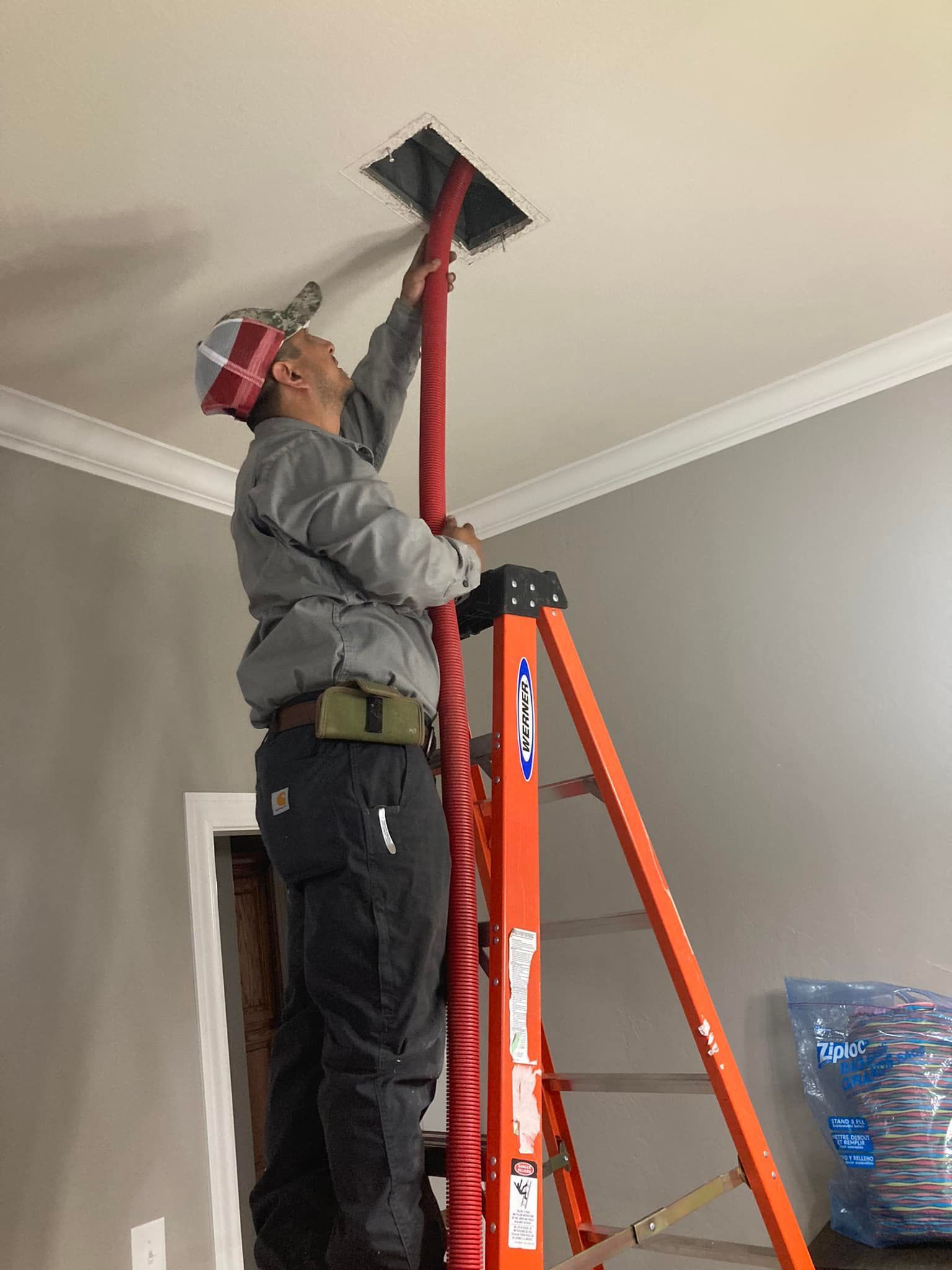 A man is standing on a ladder cleaning a hole in the ceiling.