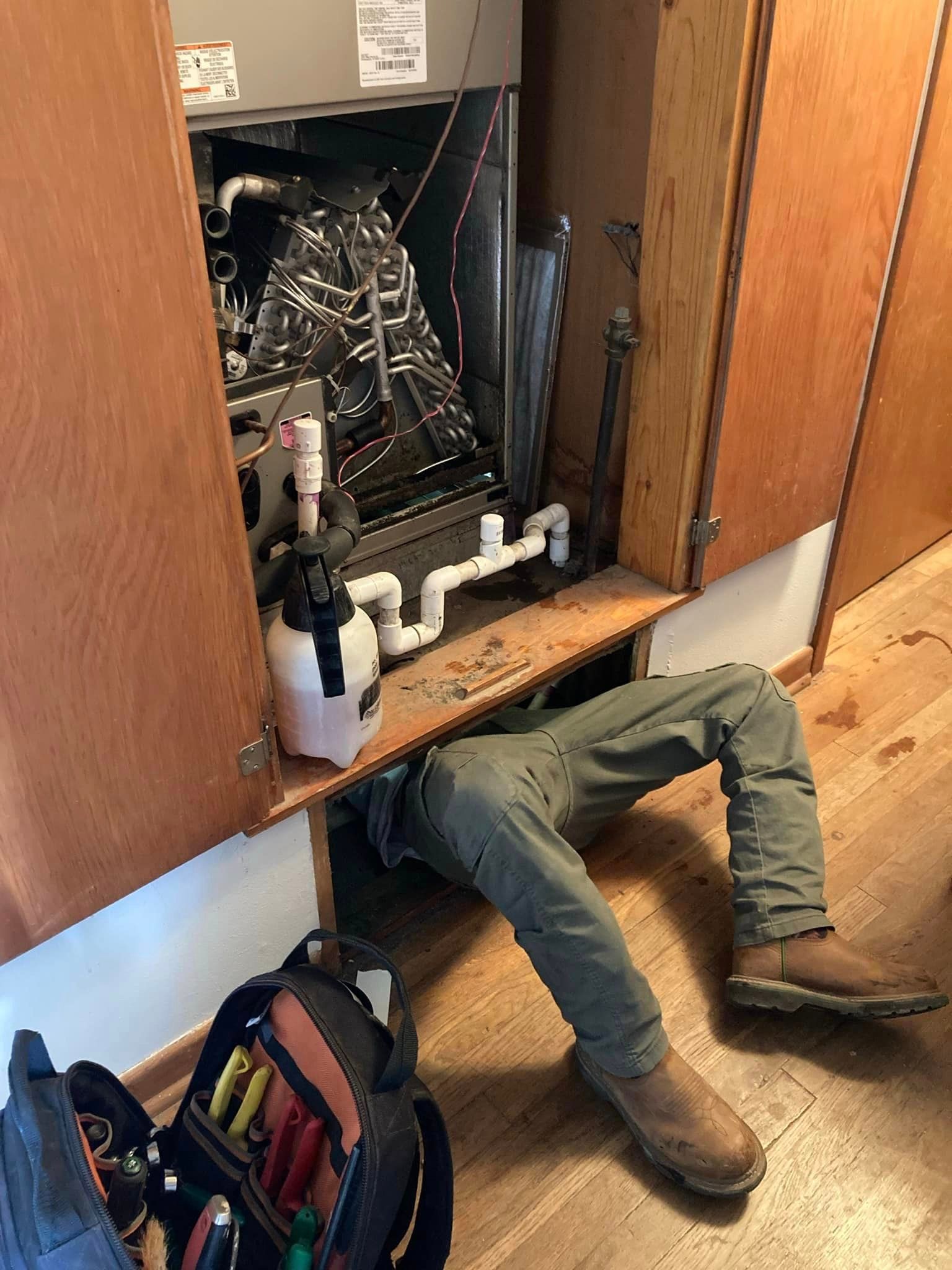 A man is crawling under a cabinet to fix an air conditioner.