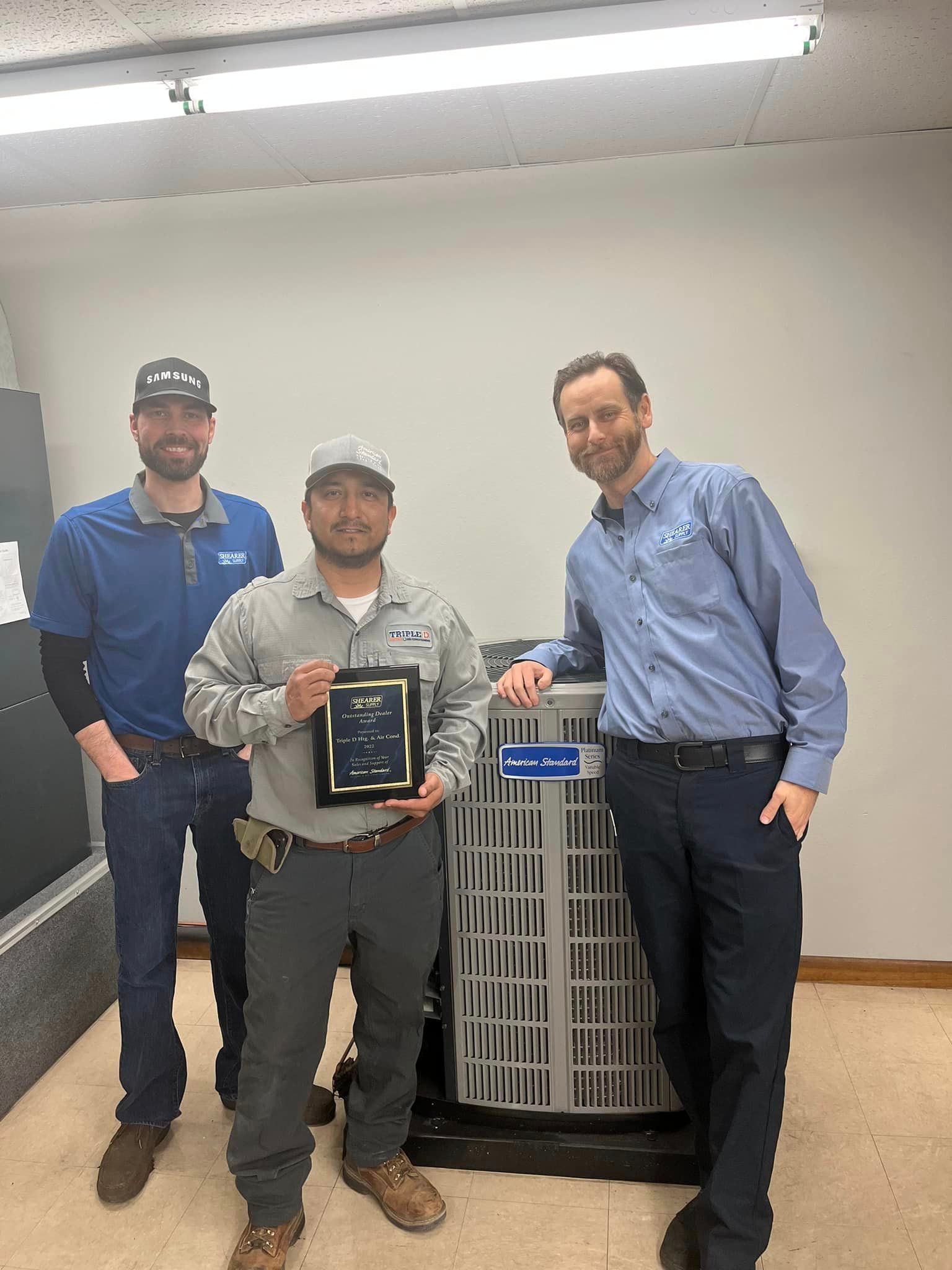 Three men are standing next to each other in front of an air conditioner holding a plaque.