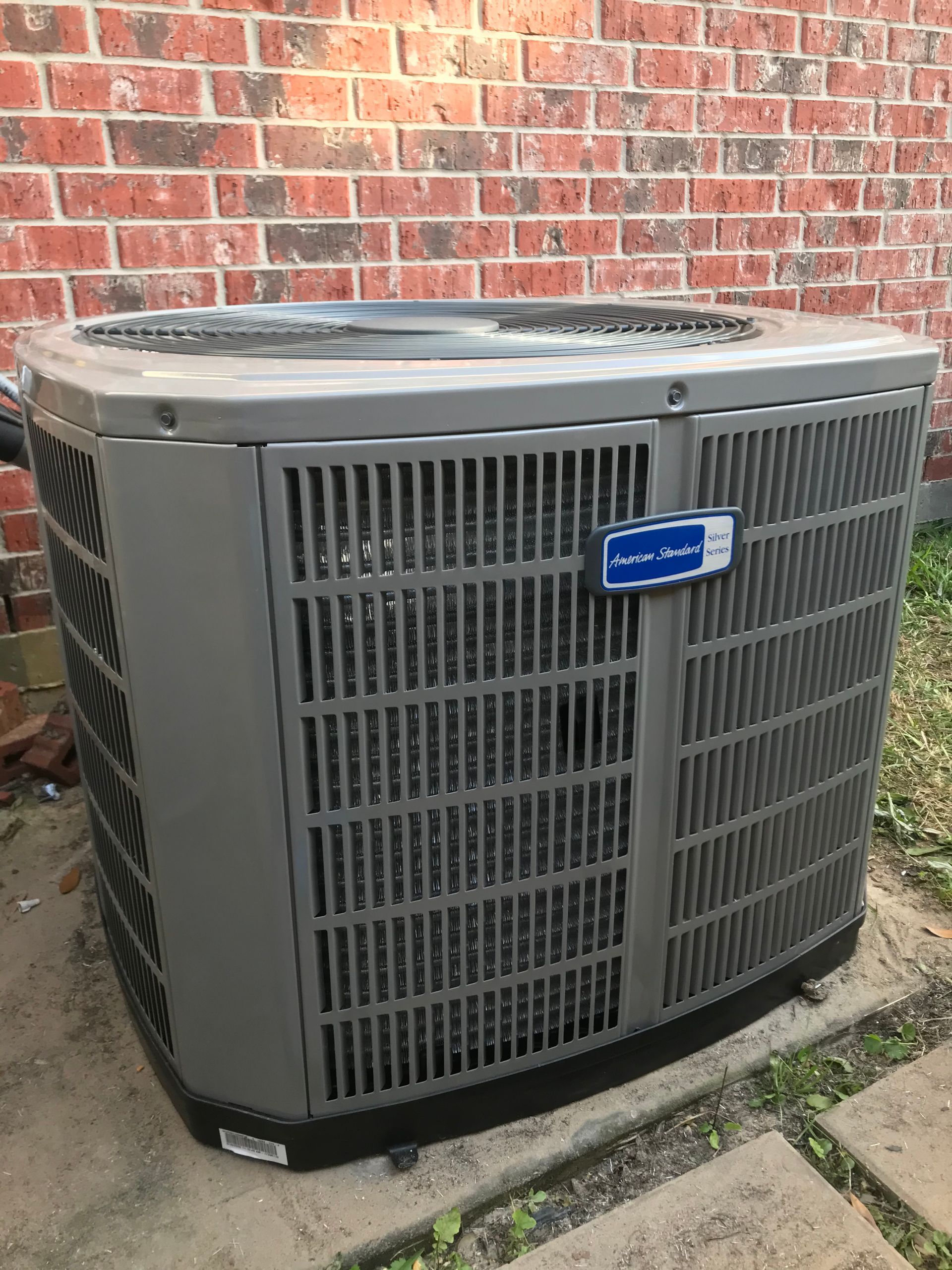 A large air conditioner is sitting in front of a brick wall.